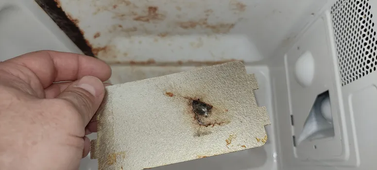 Burnt and stained microwave waveguide cover inside the cooking cavity, a common cause of sparking and arcing